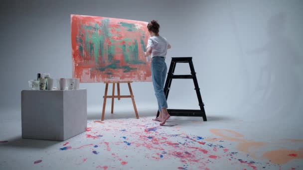 Künstlerin zeichnet mit einem Pinsel auf einer großen Leinwand in einem weißen Raum, ein talentierter Künstler zeichnet eine Farbe rote Abstraktion, moderne Kunst in der Ölmalerei. — Stockvideo
