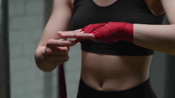 Mulher anônima lutadora envolve suas mãos com ligaduras de boxe vermelho, dia de treinamento de kickboxing em um ginásio. — Vídeo de Stock