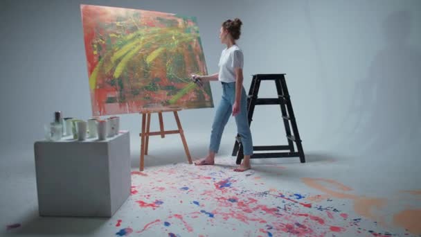 Artista femenina dibuja con pintura en aerosol en un gran lienzo en una habitación blanca, un artista talentoso dibuja una abstracción de color. — Vídeo de stock