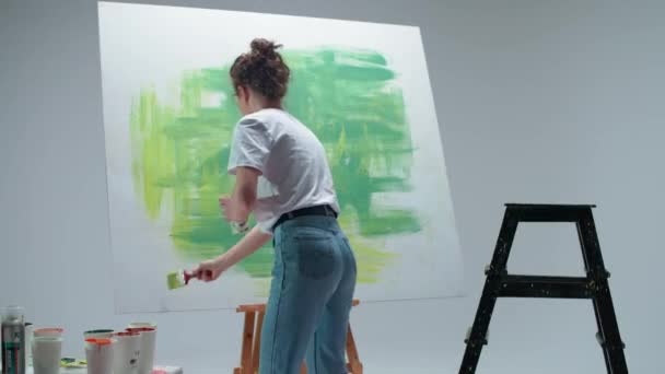 Kobieta artystka rysuje pędzlem na dużym płótnie w białym pokoju, utalentowany artysta rysuje zielony abstrakcji koloru, sztuka nowoczesna w malarstwie olejnym. — Wideo stockowe