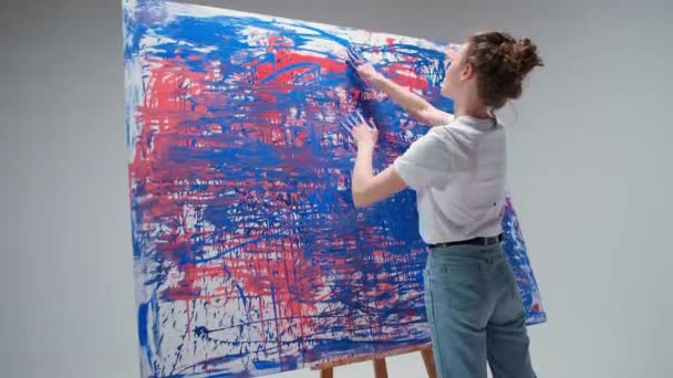 Νεαρή γυναίκα καλλιτέχνης ζωγραφίζει με τα χέρια της σε ένα μεγάλο καμβά σε ένα λευκό δωμάτιο, ένας ταλαντούχος καλλιτέχνης αντλεί ένα χρώμα αφαίρεσης, σύγχρονη τέχνη στη ζωγραφική πετρελαίου, 4k αργή κίνηση. — Αρχείο Βίντεο