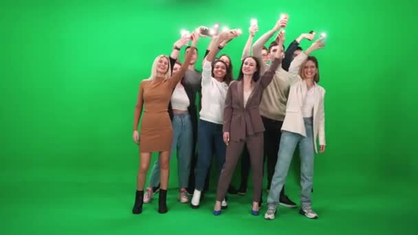 Een menigte mensen van verschillende leeftijden die dansen op een muziekconcert, mensen met beschermende medische maskers met smartphones met zaklampen aan, ze dansen en zwaaien met hun armen op een groene achtergrond, evenement — Stockvideo
