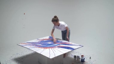 Kadın sanatçı ellerini beyaz bir odada büyük bir tuvale koyar, yetenekli bir sanatçı mavi bir soyutlama, modern sanat, üst görünüm çizer..