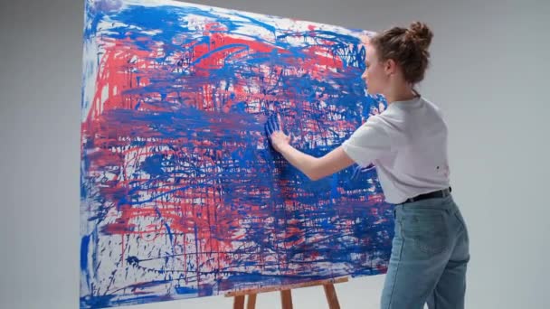 Jeune femme artiste dessine avec ses mains sur une grande toile dans une salle blanche, un artiste talentueux dessine une abstraction de couleur, l'art moderne dans la peinture à l'huile, 4k ralenti. — Video
