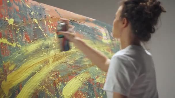 Visão traseira, artista feminina desenha com tinta spray em uma tela grande em uma sala branca, um artista talentoso desenha uma abstração de cor. — Vídeo de Stock