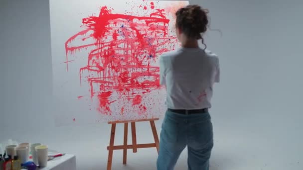 Female artist draws by splashing paint on a large canvas in a white room, a talented artist draws a color red abstraction. — Video Stock