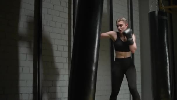 Kickboxning, aggressiv kvinna fighter tränar sina slag, slår en slagsäck, träningsdag i boxning gym, styrka passform kropp. — Stockvideo