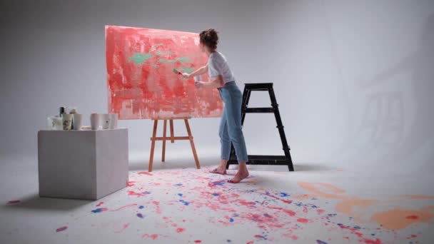 Powolny ruch, artystka rysuje pędzlem na dużym płótnie w białym pomieszczeniu, utalentowany artysta rysuje czerwony abstrakcji koloru, sztuka nowoczesna w malarstwie olejnym. — Wideo stockowe