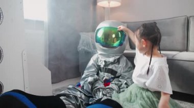 Asyalı çocuklar evdeki oturma odasında oynuyorlar, astronot kostümlü bir çocuk kız kardeşiyle yerde oturuyor, çocuklar güneş sisteminin oyuncak modeliyle oynuyorlar, 4k yavaş çekim..