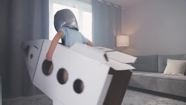 Junge im Astronautenkostüm spielt mit einer Raumfähre aus Pappe, rennt durch den Raum, 4k Zeitlupe. — Stockvideo