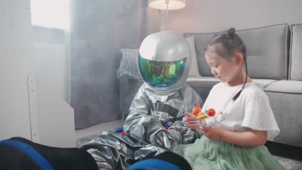 Bambini asiatici giocano in salotto a casa, un ragazzo in costume da astronauta seduto sul pavimento con sua sorella, bambini che giocano con un modello giocattolo del sistema solare, 4k rallentatore. — Video Stock