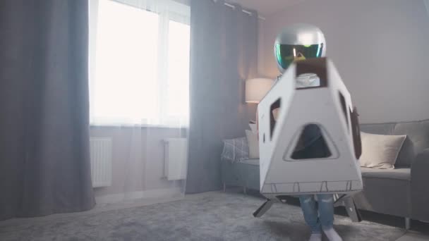 เด็กชายในชุดนักบินอวกาศเล่นกับกระดาษแข็งกระสวยอวกาศวิ่งไปรอบ ๆ ห้องเคลื่อนไหวช้า 4k . — วีดีโอสต็อก