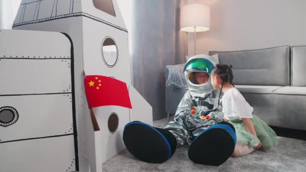 Bambini asiatici giocano in salotto a casa, un ragazzo in costume da astronauta seduto sul pavimento con sua sorella, bambini che giocano con un modello giocattolo del sistema solare. — Video Stock