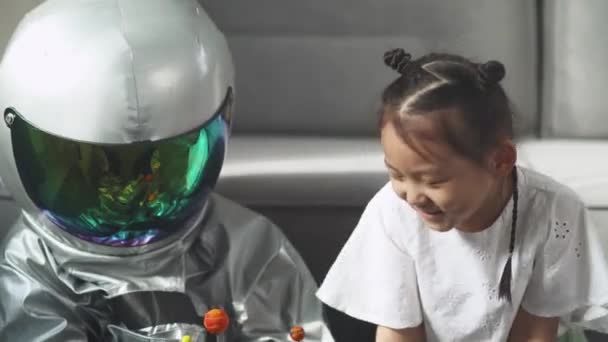 Asiatiska barn leker i vardagsrummet hemma, en pojke i en astronautdräkt sitter på golvet med sin syster, barn leker med en leksaksmodell av solsystemet. — Stockvideo