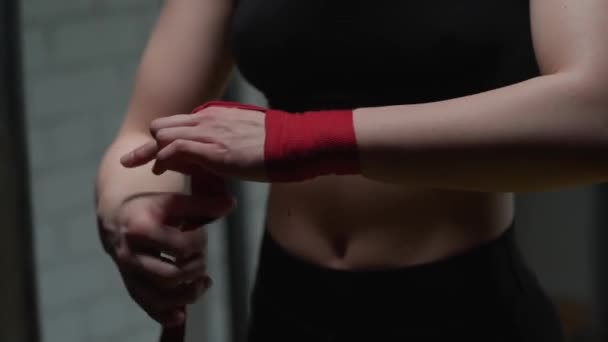 Mulher anônima lutadora envolve suas mãos com ligaduras de boxe vermelho, dia de treinamento de kickboxing em um ginásio. — Vídeo de Stock
