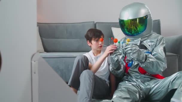 Père et fils jouent dans le salon à la maison, père en costume d'astronaute assis sur le sol avec son fils, garçon jouant avec un modèle jouet du système solaire, étude de l'astronomie, ralenti 4k. — Video