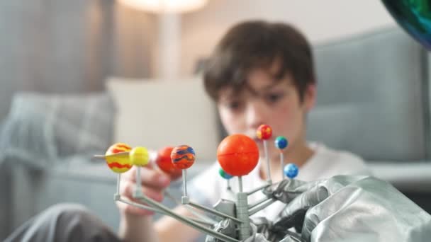 Far och son leker i vardagsrummet hemma, man i en astronaut kostym sitter på golvet med sin son, pojke leker med en leksak modell av solsystemet, studier av astronomi, 4k slow motion. — Stockvideo
