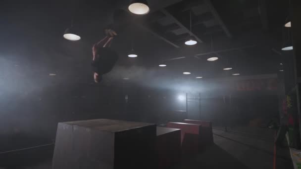 Free running, young man doing a series of somersaults on the training ground for parkour and workout, guy perform flips and gymnastic tricks in a dark space, 4k slow motion. — Vídeo de Stock