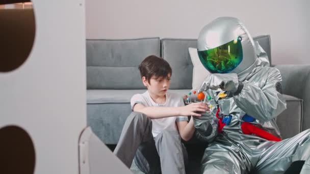 Ayah dan anak bermain di ruang tamu di rumah, ayah dalam kostum astronot duduk di lantai dengan anaknya, anak laki-laki bermain dengan model mainan tata surya, studi astronomi, gerakan lambat 4k. — Stok Video