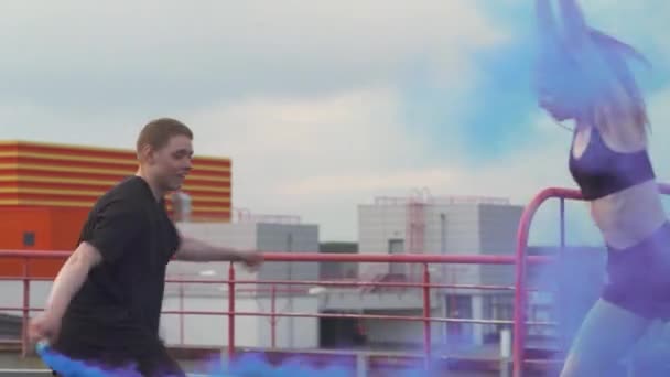 Young peoples doing a handstands and makes a flips, multi colored smoke bombs on a background, gymnastic elements and parkour on the roof of building. — Stock Video