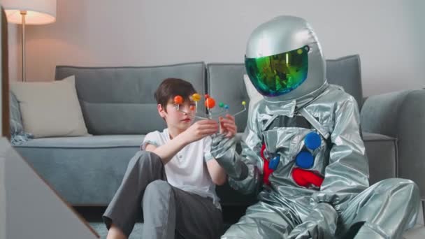 Ojciec i syn bawią się w salonie w domu, ojciec w kostiumie astronauty siedzący na podłodze z jej synem, chłopiec bawiący się zabawkowym modelem Układu Słonecznego, nauka astronomii, 4k slow motion. — Wideo stockowe