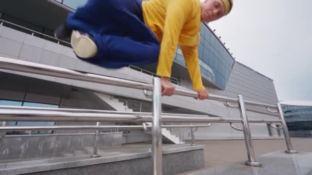 Free running, young man runs over obstacles in the city and doing a flips on training area near modern buildings, 4k slow motion. — Stock Video