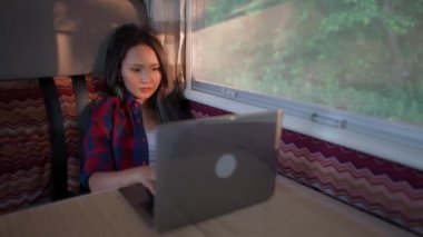 Arabada oturmuş dizüstü bilgisayar başında çalışan Asyalı bir kadın, yazı yazıyor ve uzaktan kumandalı bir iş, gün batımında bir kamp arabasının içinde portre çiziyor..