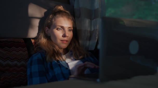 Handheld, femme travaillant à un ordinateur portable assis dans une voiture, tapant du texte et du travail à distance dans la nature, portrait dans une lumière du coucher du soleil à l'intérieur d'un camping-car. — Video