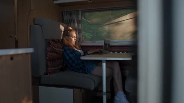 Kvinnlig frilansare arbetar på en bärbar dator medan du sitter i en bil, skriva text och fjärrarbete i naturen, porträtt i en solnedgång ljus inuti en campingbil. — Stockvideo