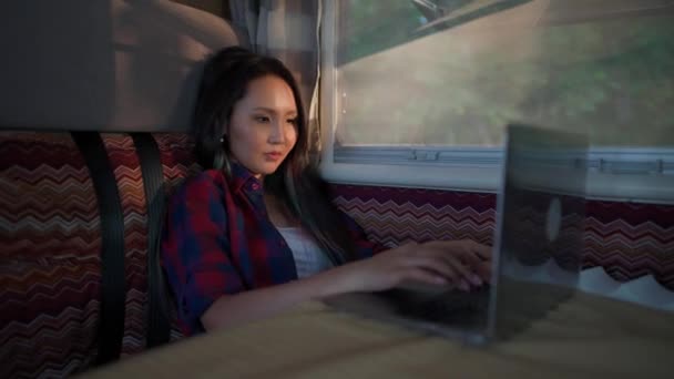 Ręczna, azjatycka kobieta pracująca na laptopie, siedząca w samochodzie, pisząca tekst i pracująca zdalnie w naturze, portret w świetle zachodu słońca w samochodzie kempingowym. — Wideo stockowe