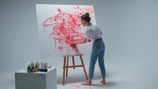 Mladá žena malířka kreslí s rukama na velké plátno v bílém pokoji, talentovaný umělec kreslí barvu červené abstrakce, kreslí tím, že stříkající barvy. — Stock video