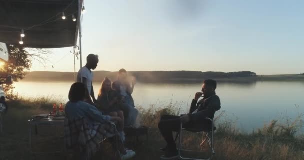 Été, groupe de jeunes profitent d'une fête dans la nature près du lac, les gens communiquent et se détendre dans la nature près du camping-car, coucher de soleil, vue de la hauteur. — Video