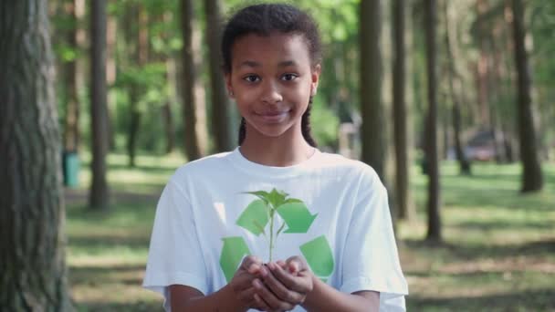 Молода африканка-доброволець тримає в руках маленьку квіткову рослину і дивиться на камеру, метафорична дія, природа в наших руках, турбота про природу, повільний рух 4k . — стокове відео