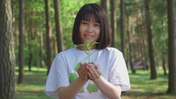 Caring for nature, young asian female volunteer holds a small flower plant in her hands and looks at the camera, a metaphorical action, nature is in our hands, slow motion. — Stock Video