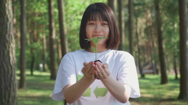 Caring for nature, young asian female volunteer holds a small flower plant in her hands and looks at the camera, a metaphorical action, nature is in our hands, 4 slow motion. — Stock Video