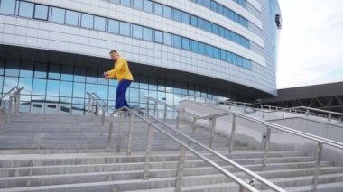 Parkour, genç adam şehirdeki engellere ters takla atıyor ve modern binaların yakınındaki eğitim alanında takla atıyor..