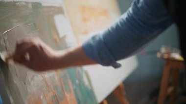 Yavaş çekim, yaratıcı kişi, yetenekli yetişkin bir sanatçı tuvali gri-bej boya ile kaplıyor, arka planı çiziyor ve ellerin yakın plan görüntüsünü çiziyor..