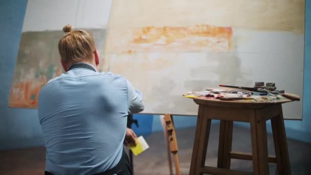 Pandangan kembali terhadap orang-orang kreatif di tempat kerja, seorang seniman laki-laki berbakat menggambar gambar abstrak di atas kanvas besar, menutupi kanvas dengan cat minyak beige. — Stok Video