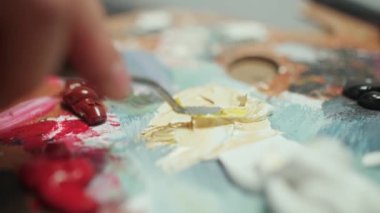 Bir sanatçı palet bıçağıyla yağlı boyayı karıştırıyor, işte yaratıcı bir insan, yakın çekim, 4K yavaş çekim..