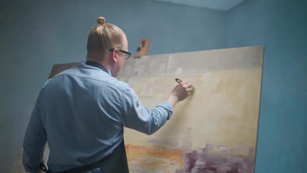 Estudio de arte, persona creativa en una camisa azul y gafas en el trabajo, un talentoso artista masculino adulto dibuja un cuadro abstracto en un lienzo grande. — Vídeos de Stock