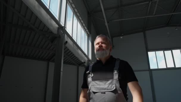 Slow motion, an adult gray-haired man worker walks through the warehouse, a working engineer walks through the territory of an empty logistics warehouse, cinematic lighting. — Stock Video