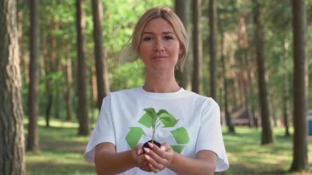 Una volontaria caucasica tiene in mano una piccola pianta di fiori e guarda la macchina fotografica, un'azione metaforica, la natura è nelle nostre mani, si prende cura della natura, al rallentatore. — Video Stock