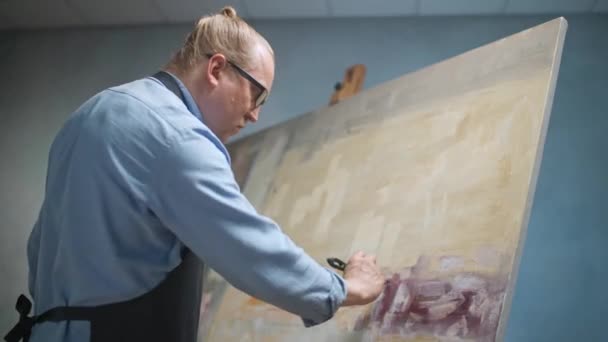 Personne créative au travail, un artiste adulte talentueux couvre la toile avec de la peinture à l'huile, amorce et dessine le fond. — Video