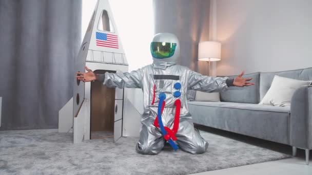 Vader en zoon spelen in de woonkamer thuis, Afrikaanse man in een pak van een Amerikaanse astronaut knuffelt zijn gelukkige zoon in de buurt van een kartonnen model van een ruimteschip, 4k slow motion. — Stockvideo