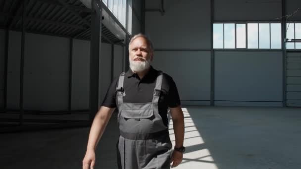 Zpomalený pohyb, dospělý šedovlasý muž prochází skladištěm, pracující inženýr prochází teritoriem prázdného logistického skladu, kinematografické osvětlení. — Stock video