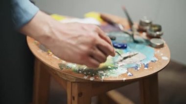Atölye çalışması, bir sanatçı palet bıçağıyla yağlı boyayı karıştırır, işte yaratıcı bir kişi, ellerin yakın çekim görüntüsü.