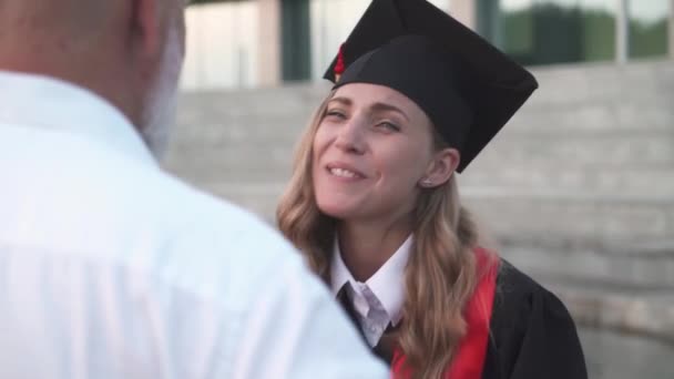 卒業式、父親が娘を抱きかかえ、大学を卒業し、卒業生のローブの女性は彼女の手に卒業証書、感情的な瞬間を保持しています. — ストック動画