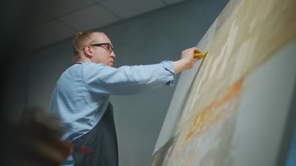 Artiesten workshop, creatief persoon aan het werk, een getalenteerde volwassen man kunstenaar bedekt het doek met beige olieverf, tekent het moderne abstracte beeld, lage hoek uitzicht, 4k slow motion. — Stockvideo