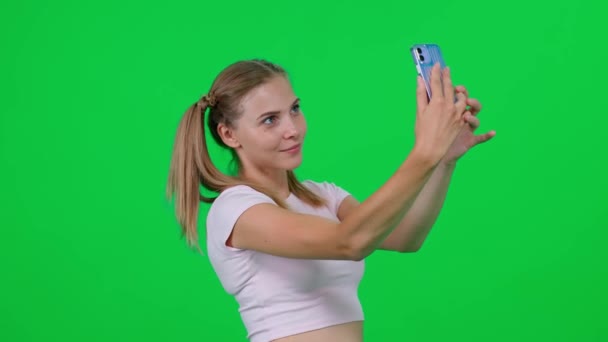 Smuk kaukasisk kvinde tager en selfie på en smartphone, ung kvinde tager billeder af sig selv på en grøn baggrund, en kroma nøgle skabelon. – Stock-video