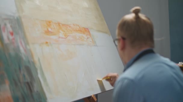 Vista posterior de la persona creativa en el trabajo, un talentoso artista masculino dibuja un cuadro abstracto en un lienzo grande, cubre el lienzo con pintura al óleo beige, 4k cámara lenta. — Vídeos de Stock